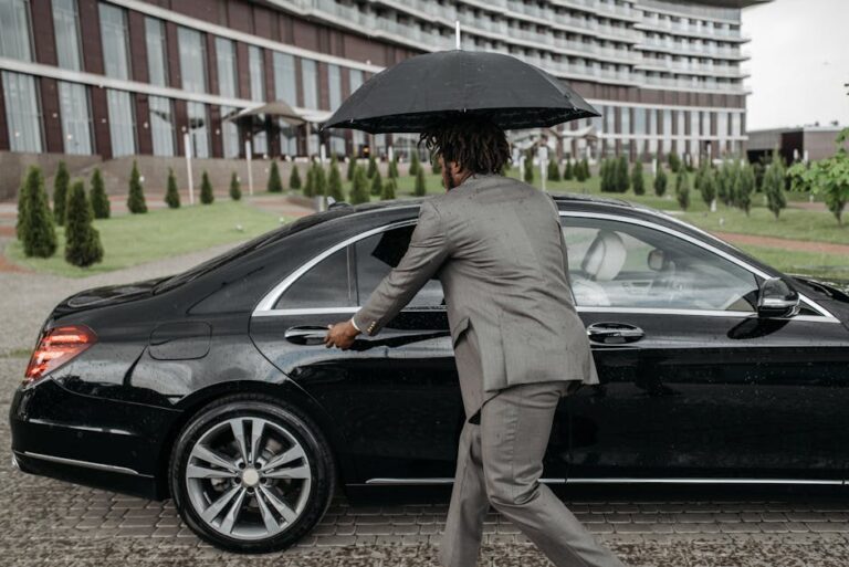 A man in a suit opening a car door while holding an umbrella in the rain.